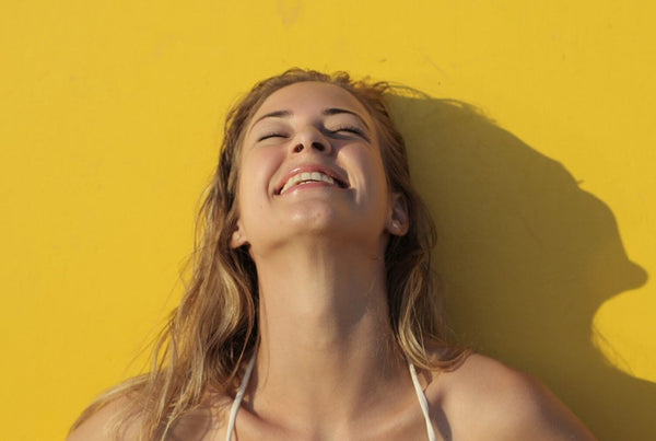 frau lächelt mit geschlossenen augen kopf nach oben geneigt und bräunt sich in der sonne tanning gelber hintergrund starker schattenwurf frau silhouette linke seite